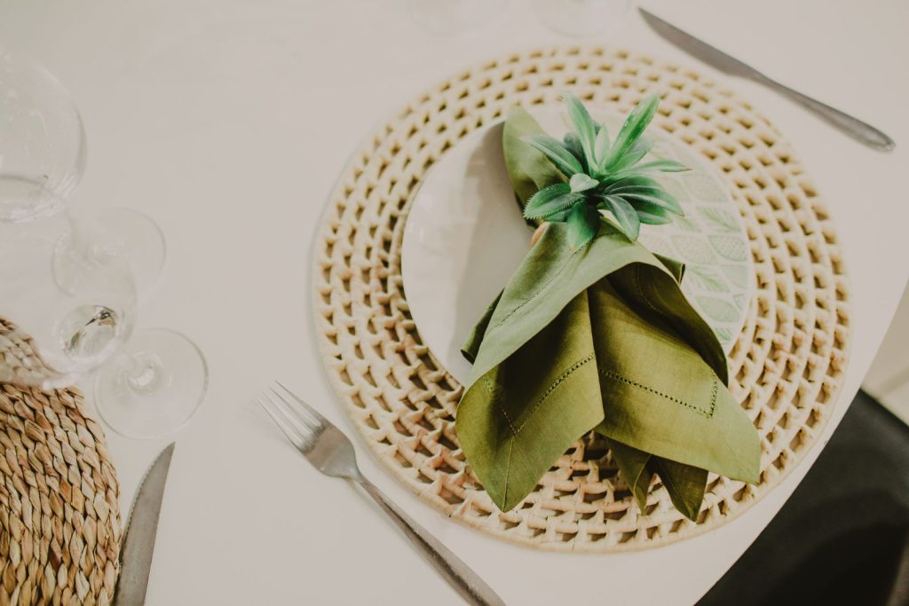 From above composition of green napkin in holder served on white plate on place mat near wineglasses before banquet