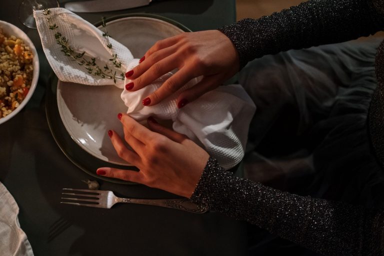 Close-up of hands elegantly arranging a napkin on a plate, capturing a moody dining atmosphere.