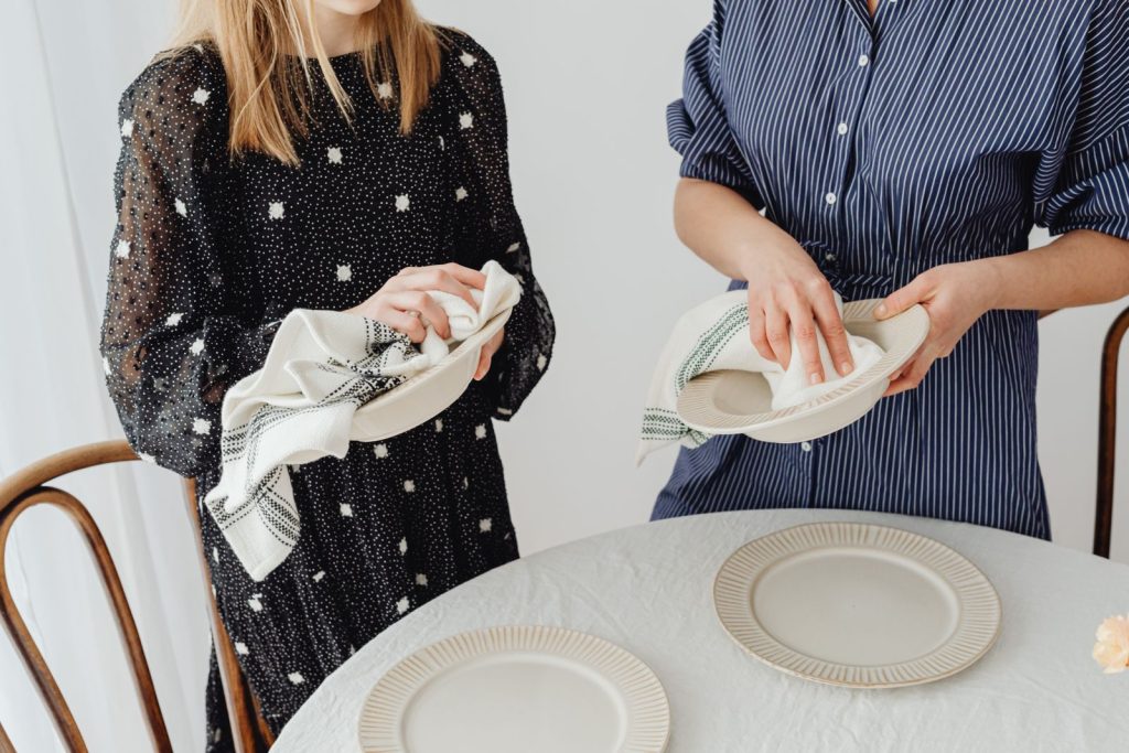 Women drying ceramic bowls and setting a table with plates and napkins.