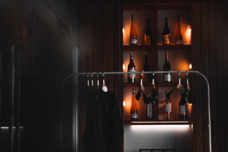 Chic bar with backlit bottles and clothing rack in dim lighting, exemplifying modern aesthetics.