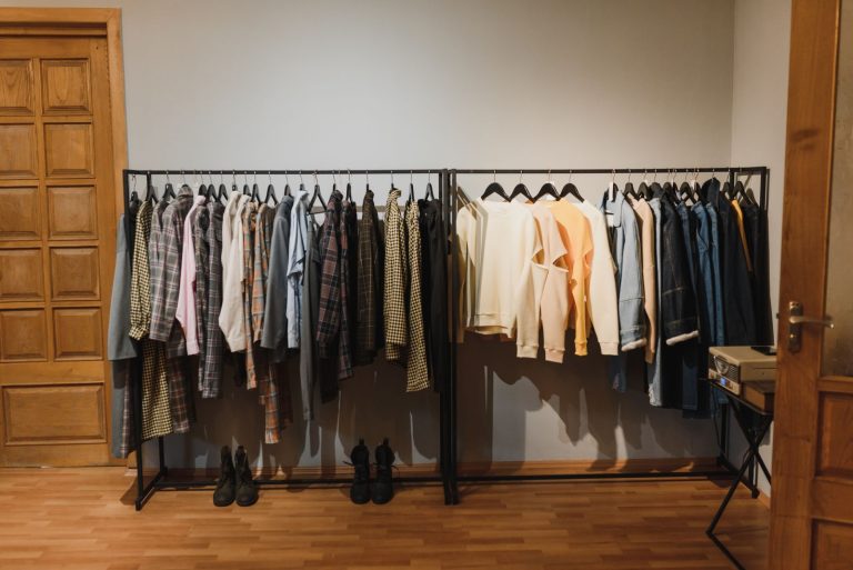 A neatly arranged indoor clothing rack with various garments on hangers in a wooden-floored room.
