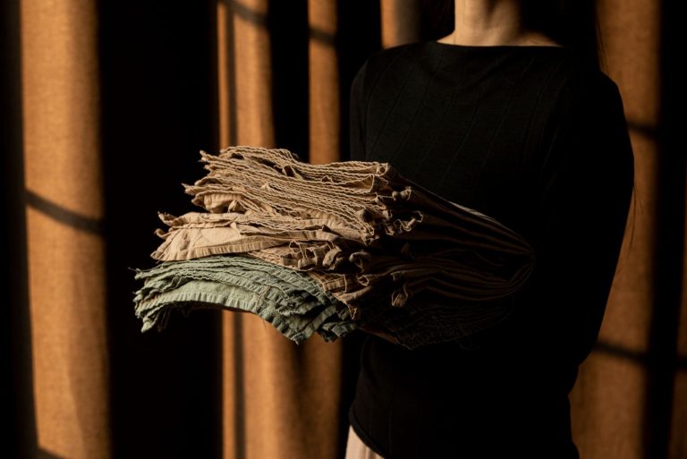 A woman holds folded fabric with textured lines in artistic shadows indoors.