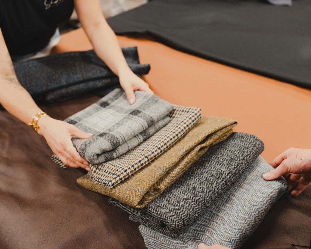Close-up of hands organizing various patterned tweed fabrics in a tailor shop setting.
