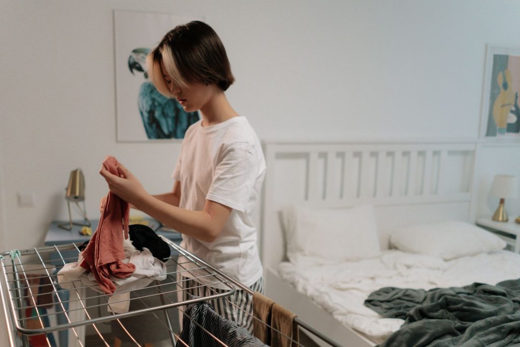 Woman folding clothes in a tidy bedroom with white decor and soft lighting.