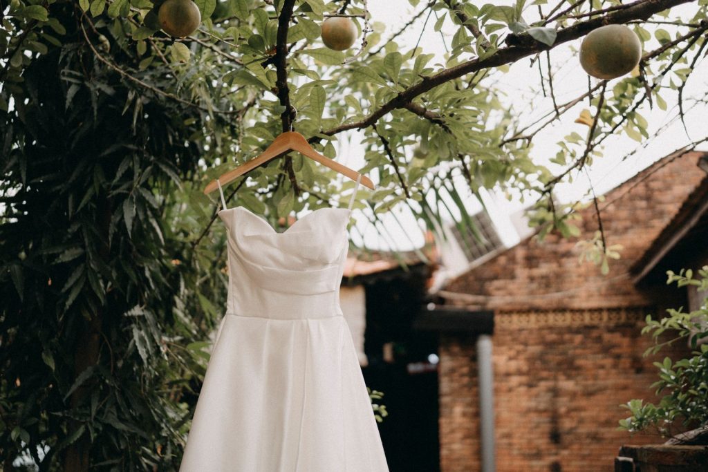 A beautiful wedding dress hanging on a branch outdoors, surrounded by lush greenery.