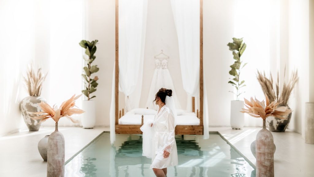 A serene bridal suite featuring a bride in a dressing gown, set against a luxurious interior with a canopy bed.