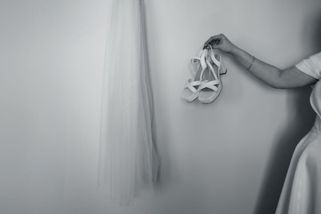 Monochrome image of bridal veil and shoes held by a bride, evoking elegance and simplicity.