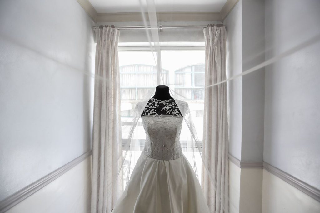 Lace wedding dress displayed elegantly on a mannequin near a large window, creating a soft and luxurious ambiance.