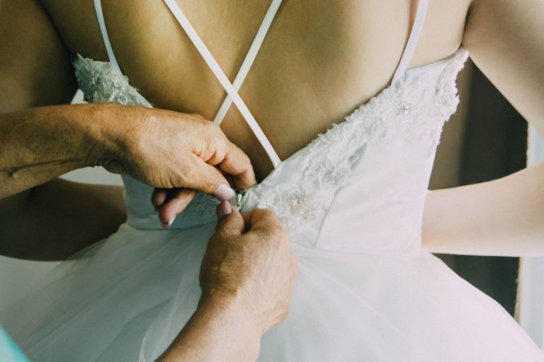 A close-up of a bride's dress being fastened, showcasing elegant lace details and wedding preparation.