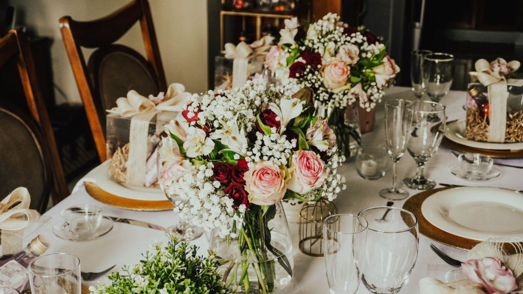 Beautifully decorated wedding table with rose bouquets and elegant dinnerware setup.