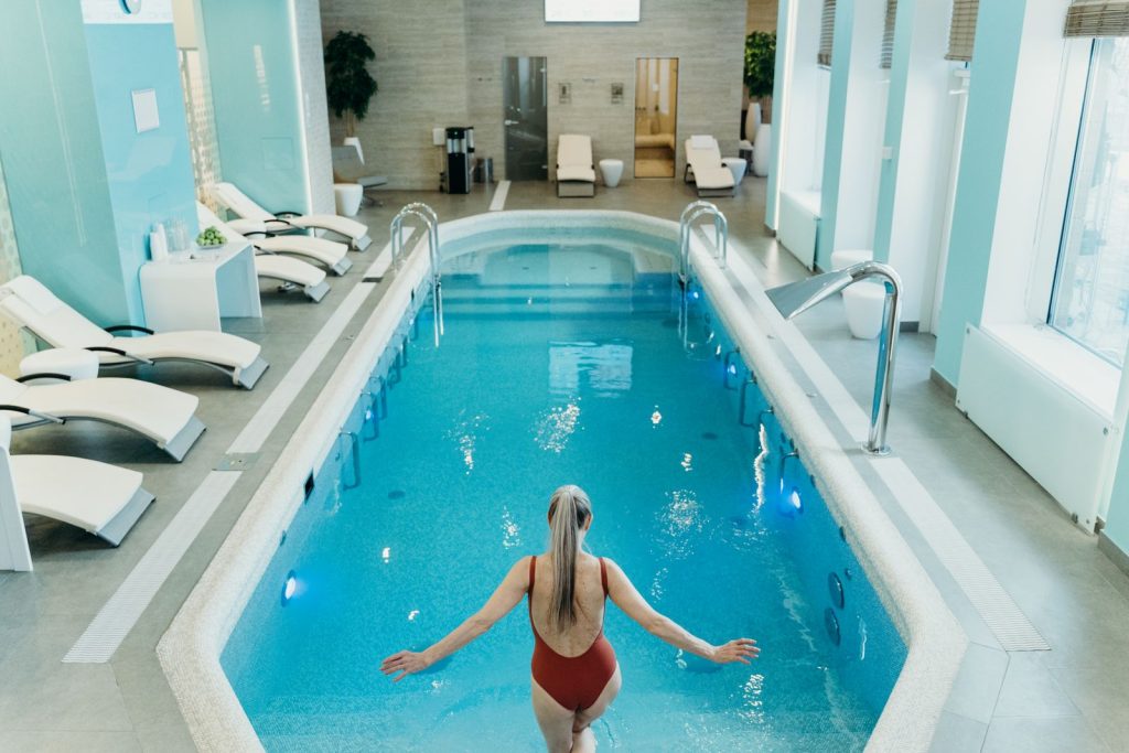 A woman in a red swimsuit prepares to enter an elegant indoor pool at a luxurious spa.