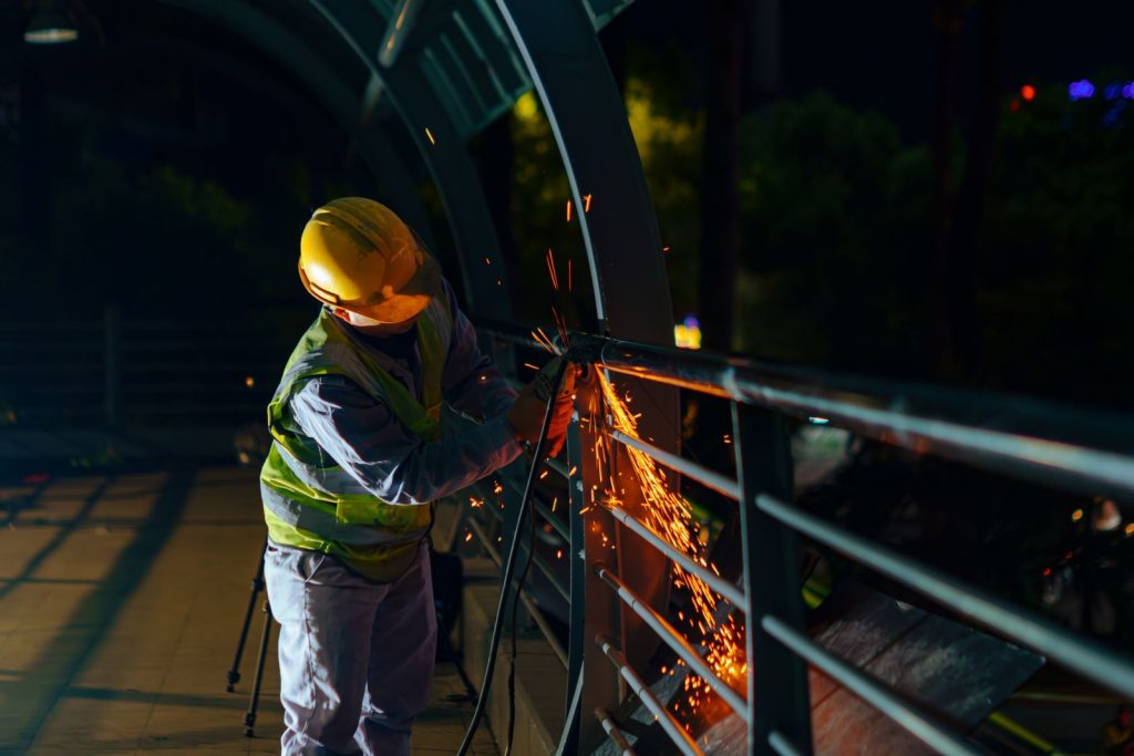 Construction worker welding a bridge at night in Ho Chi Minh City, Vietnam, with sparks flying.
