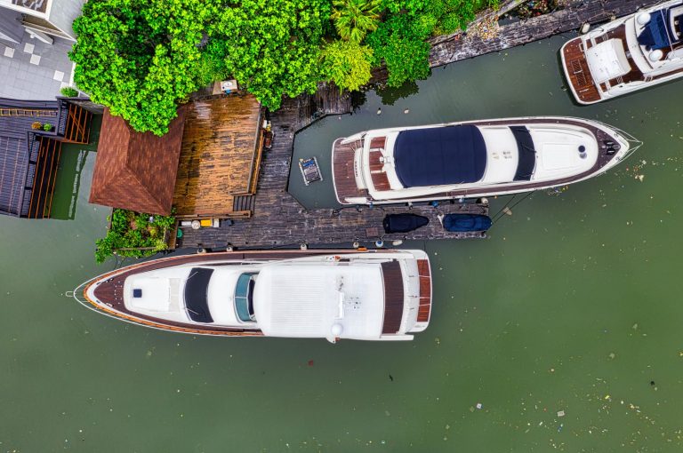 Overhead view of luxury yachts and a wooden pier in Jakarta, surrounded by lush green trees.