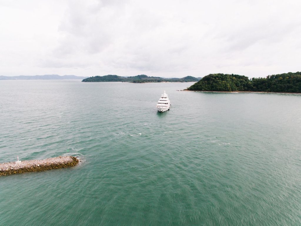Aerial view of a luxury yacht sailing near lush islands under a cloudy sky.