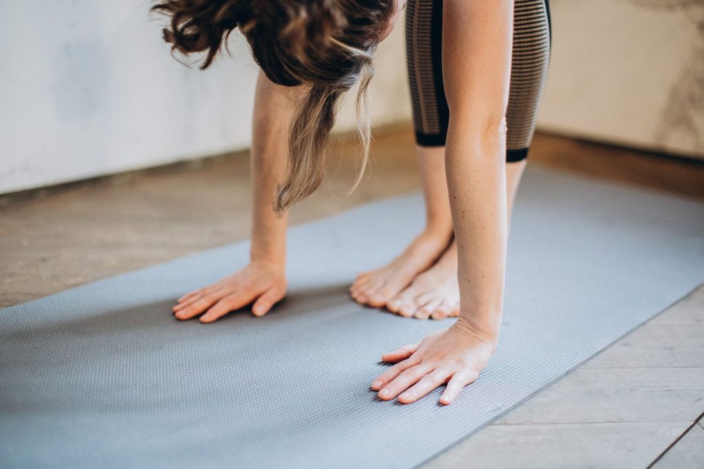 An adult woman performing a forward bend yoga pose indoors on a mat, focusing on flexibility and concentration.