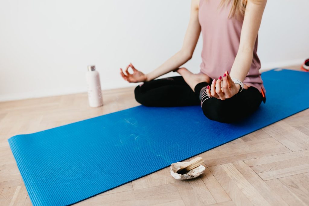 Anonymous slim female meditating alone in pose of lotus while sitting on rubber blue mat