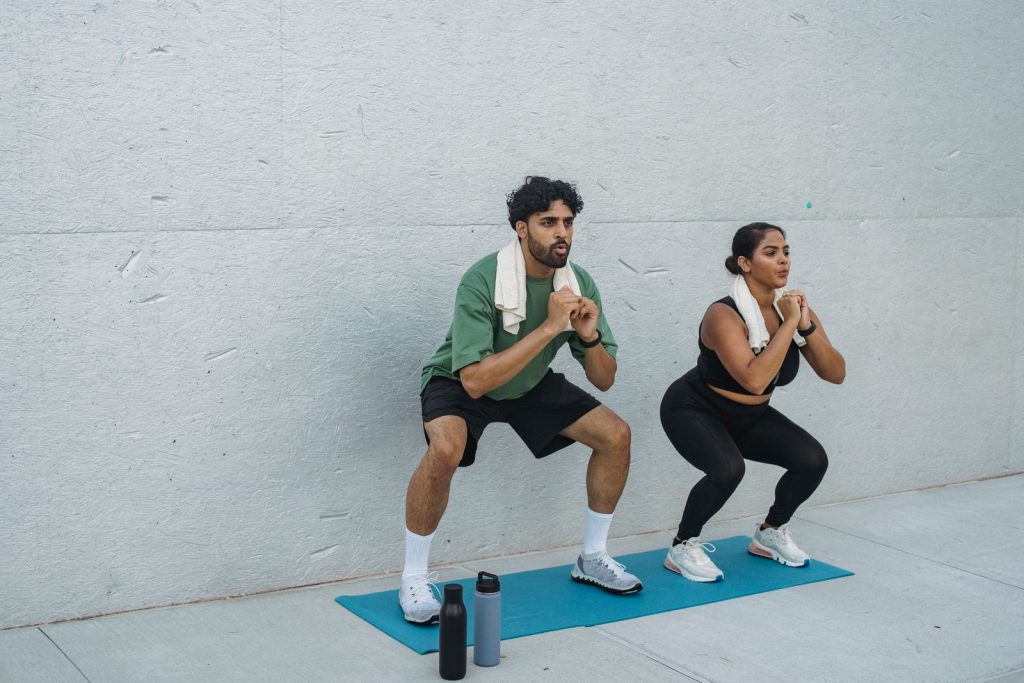 Focused couple performing squats outdoors on yoga mat, showcasing teamwork and healthy lifestyle.