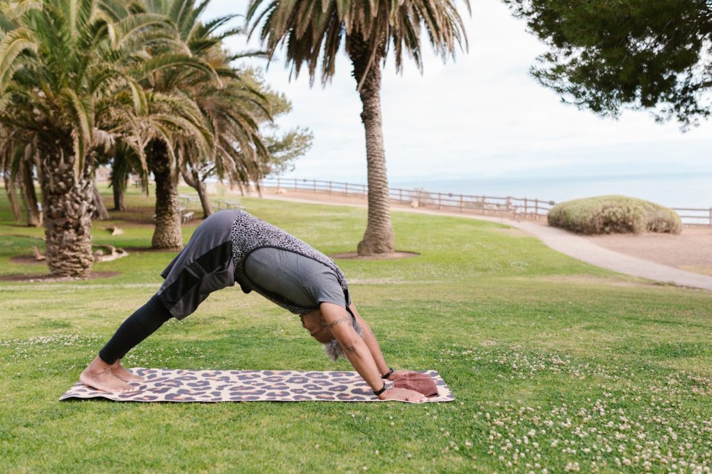 Adult male practicing yoga pose on mat in scenic park with palm trees.