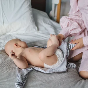 Crop woman dressing baby on bed