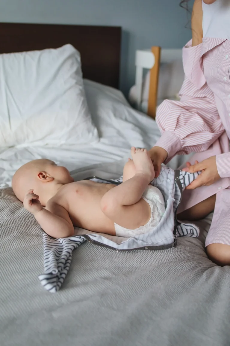 Crop woman dressing baby on bed