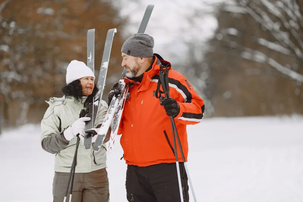 Man and woman wearing winter jackets holding skis