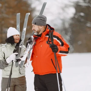 Man and woman wearing winter jackets holding skis