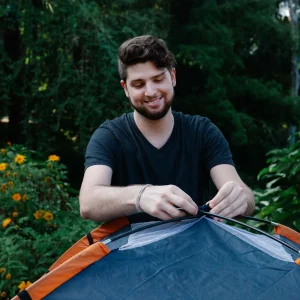 Smiling hiker setting up tent in campsite